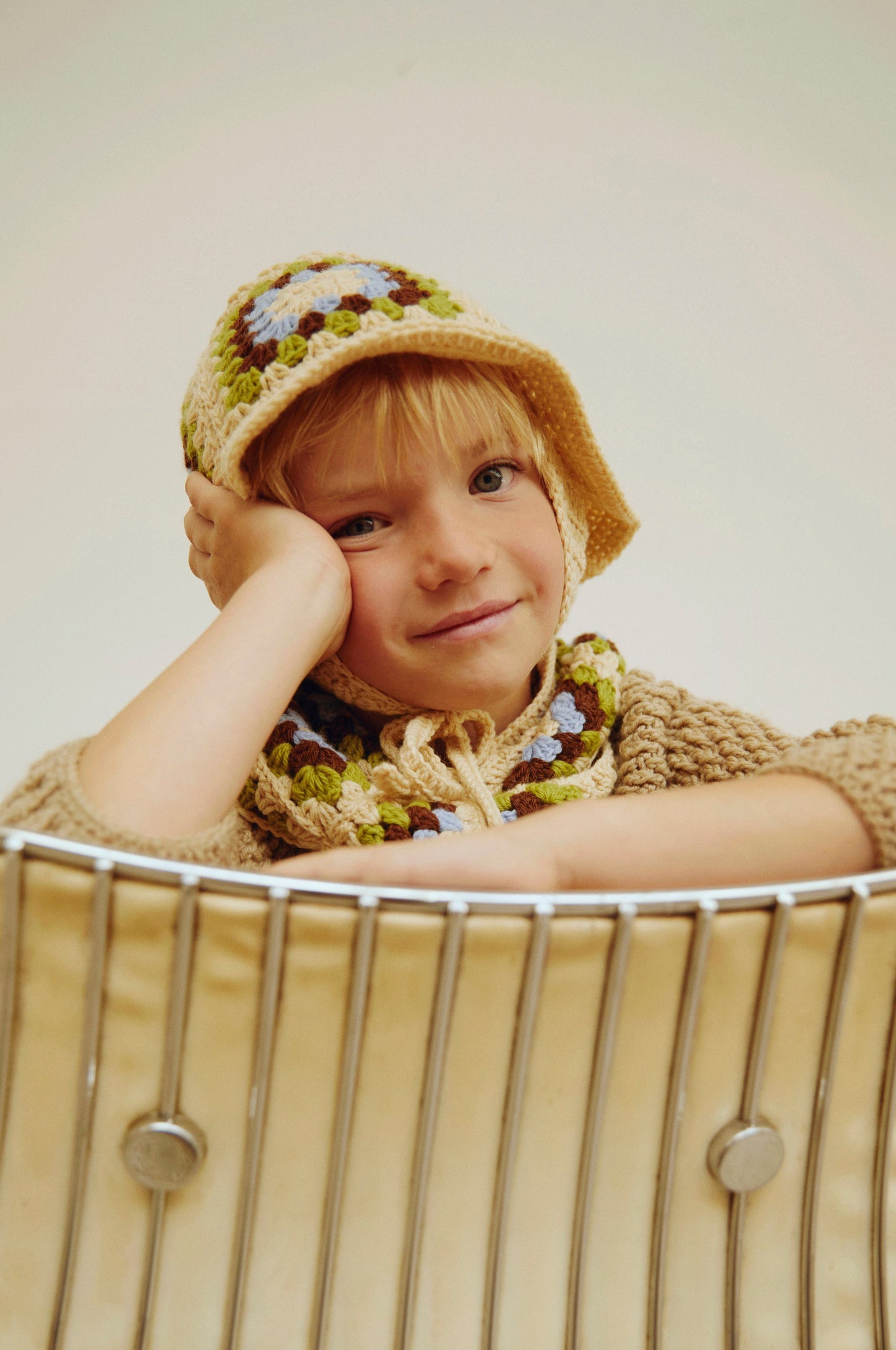 Child wearing a knitted hat and sweater sitting in a wire basket.