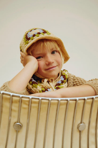 Child wearing a knitted hat and sweater sitting in a wire basket.